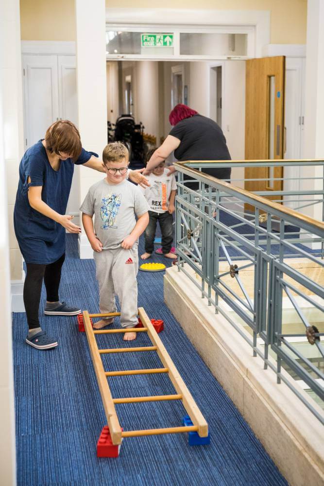 Child stepping through a ladder on the floor, supported by a teacher