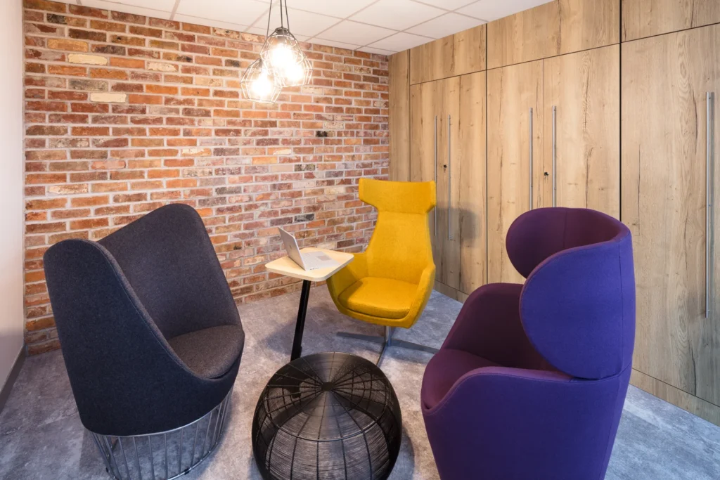 A modern office meeting room with an exposed brick wall, abstract chairs & wooden cabinetry