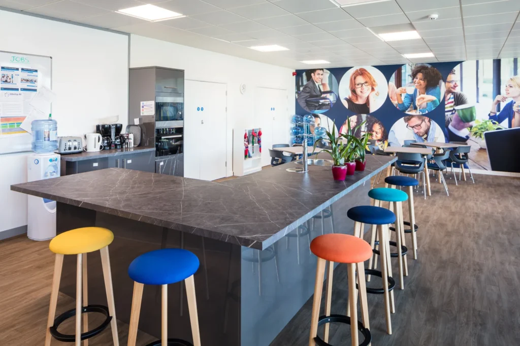 Modern kitchen area with L-shaped marble table, chairs, and decorative wall featuring employee photos