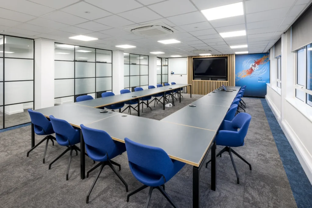 Large modern meeting room with TV, glass partitions, and office seating