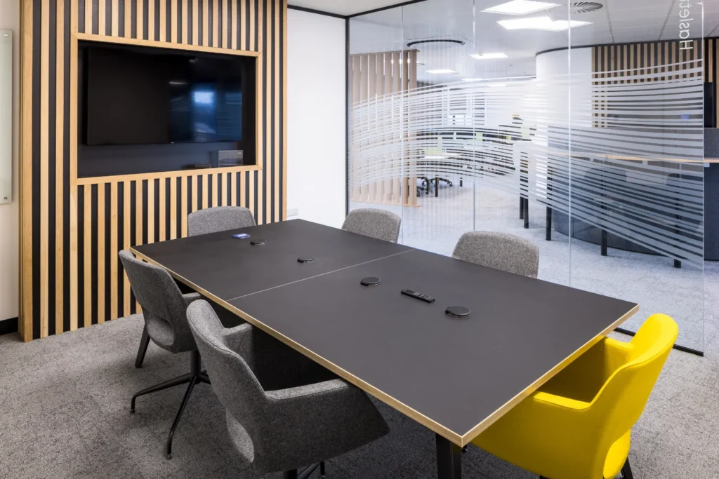Large modern meeting room with TV, glass partitions, and office seating