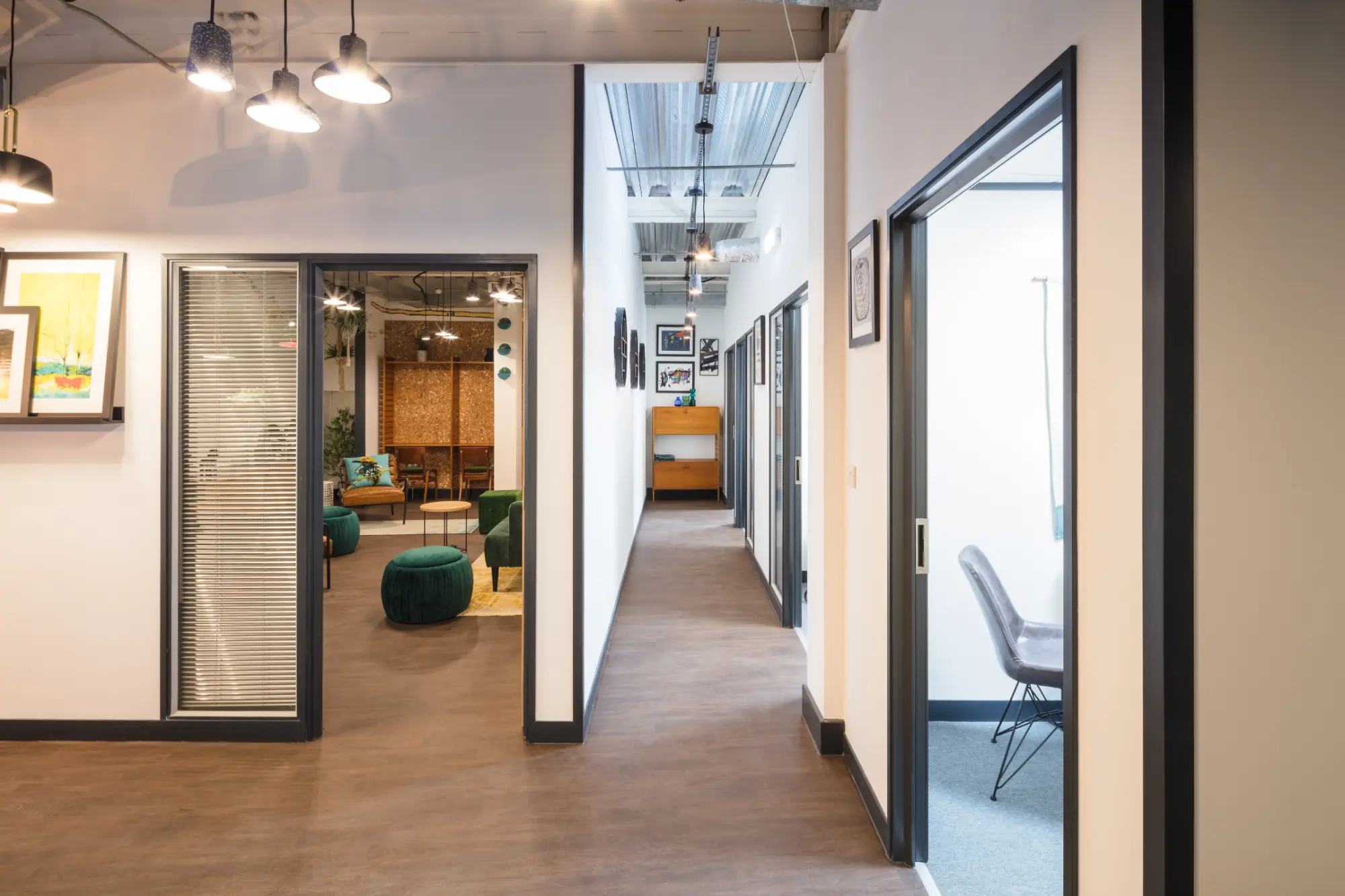 "Modern office space with multiple rooms, contemporary lighting, and wall art. View into a meeting room with table and chairs, featuring clean white walls and a polished floor."