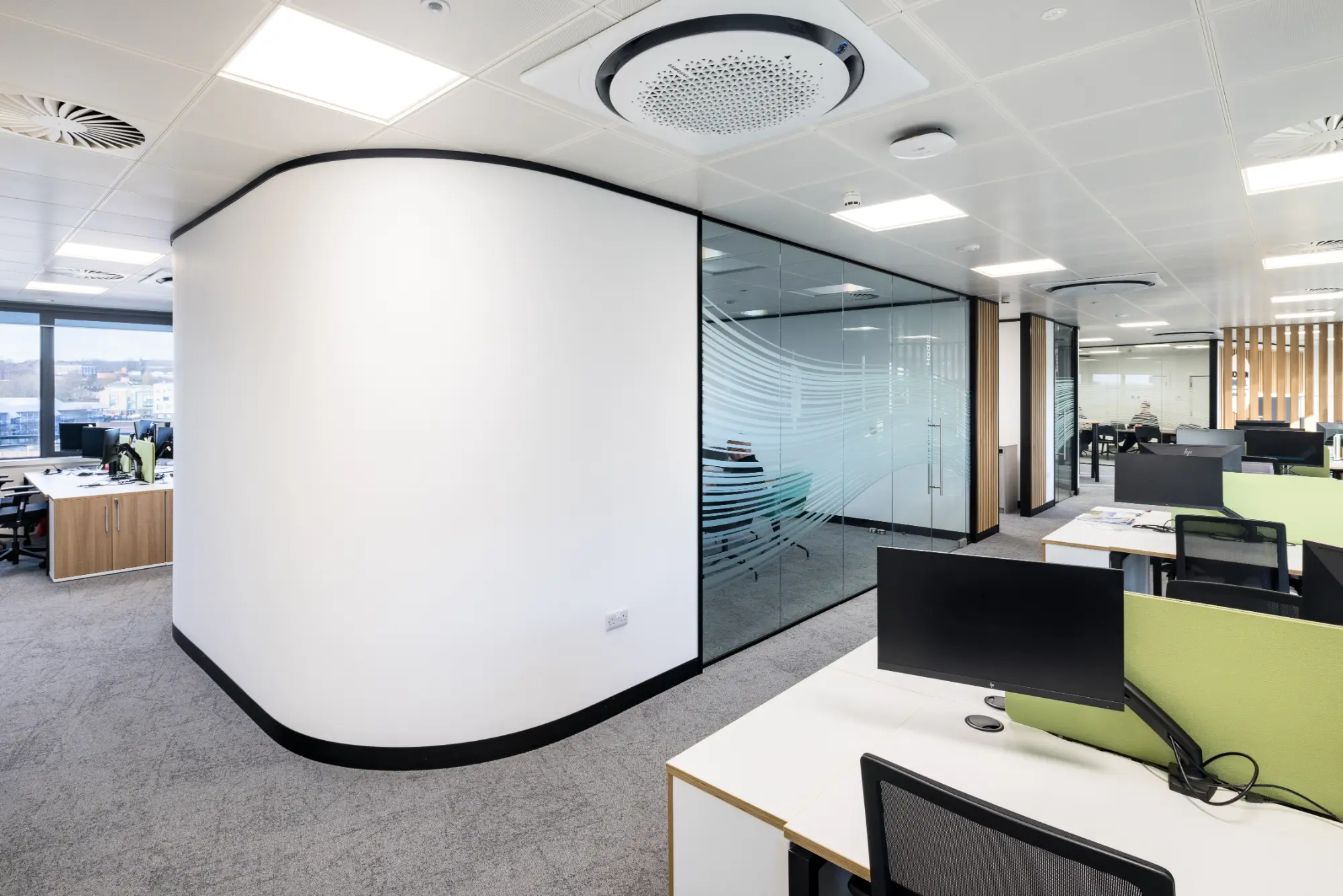 Open office space with desks and chairs, surrounded by multiple meeting rooms featuring glass partitions.